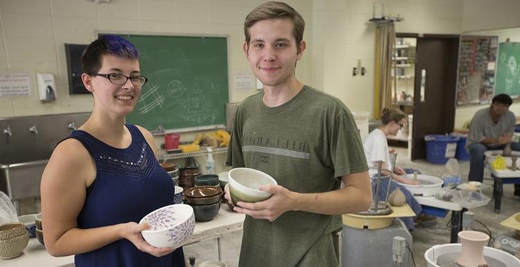 Showing off some of the soup bowls created and donated by USA to benefit Art Soup are Eric Jager, visual arts major, and Alana Kruse, ceramics lab assistant.